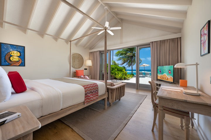 Modern bedroom with a view of the ocean, palm trees, and a desk.
