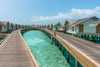 Water bungalows with wooden walkways over clear blue water on a sunny day.