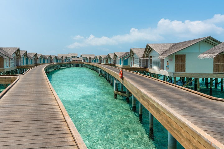 Water bungalows with wooden walkways over clear blue water on a sunny day.