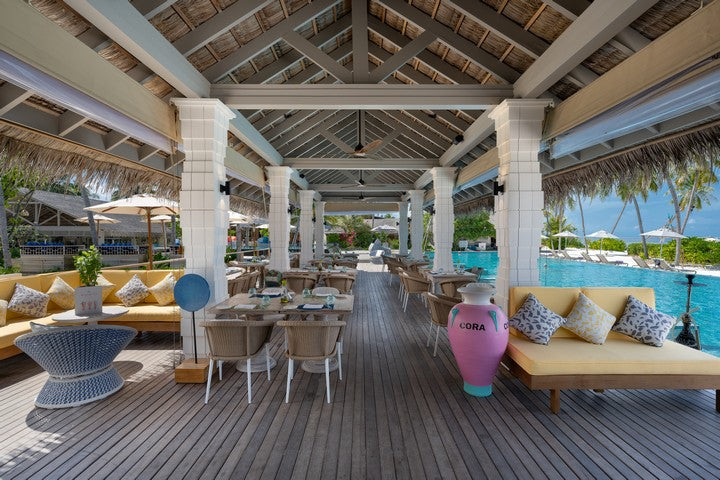 Outdoor lounge area with tables, chairs, and a pool in the background