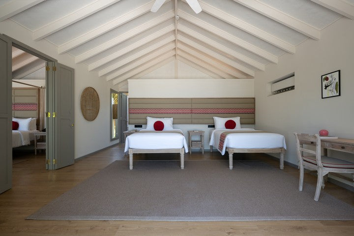 Bedroom with two beds, a table, and chairs under a vaulted ceiling.