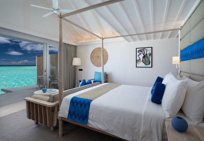 Modern bedroom with a large bed, blue accents, and a view of the ocean.