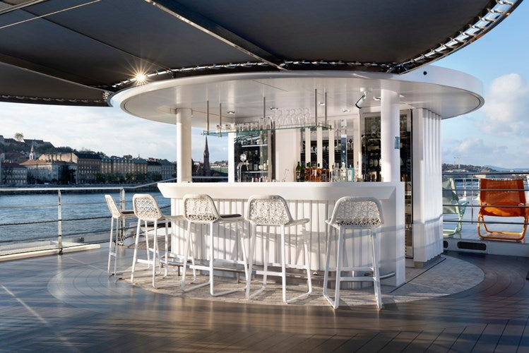 Modern outdoor bar area with white chairs and tables on a deck with a cityscape in the background.