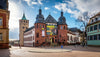Historic building with a clock tower and people walking around in a town square.