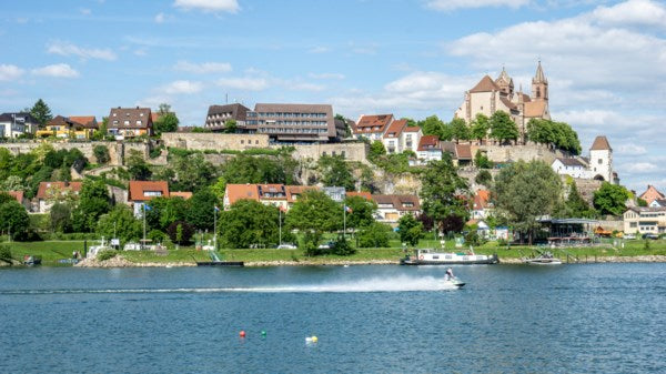 Town on a hill overlooking a river with boats, under a blue sky with clouds.