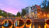 Evening view of a canal with illuminated bridge and traditional Dutch houses in Amsterdam.