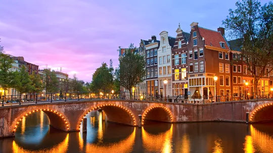 Evening view of a canal with illuminated bridge and traditional Dutch houses in Amsterdam.