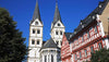 Two tall church towers with a clear blue sky and traditional buildings in the foreground.