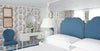 Decorative bedroom with blue upholstered headboard, floral arrangement, and patterned wallpaper.