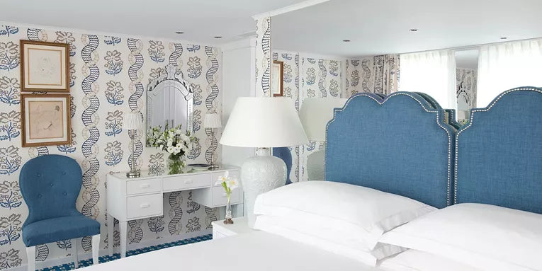 Decorative bedroom with blue upholstered headboard, floral arrangement, and patterned wallpaper.